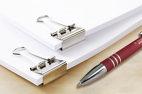 The image shows several documents on a table given to customers together with promotional pens.