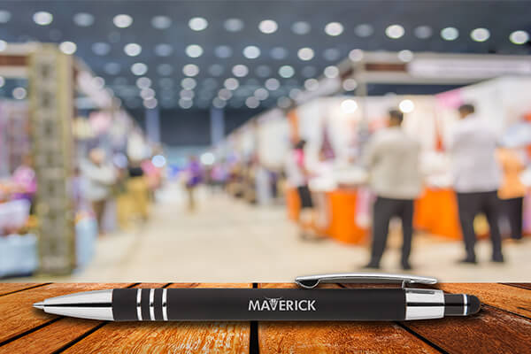 A brand spokesman from a company distributes promotional pens to interested parties at a trade fair stand.